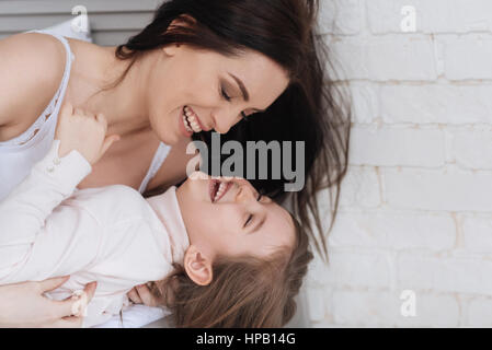 Des émotions positives. Cheerful belle mère tenant sa fille et de rire tandis que passer du temps avec sa Banque D'Images