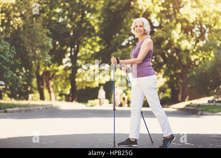 Rester en bonne santé. Jolie femme âgée positive holding polonais et de marcher tout en faisant des activités sportives dans le parc Banque D'Images