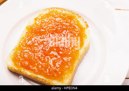 Le pain avec confiture orange pêche dans une assiette sur tableau blanc Banque D'Images