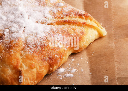 Petit pain frais avec du sucre en poudre sur un papier d'emballage Banque D'Images