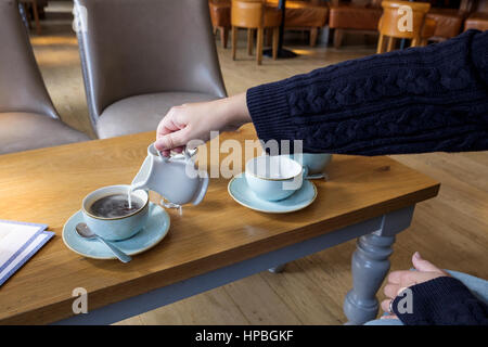 Une femme dans un café est représenté le lait en versant une tasse de café Banque D'Images