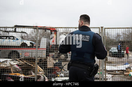 Un état policier se place en avant de la clôture à une propriété commerciale alors qu'une dépanneuse remorques loin une voiture rouillée dans le quartier de Gutleutviertel à la périphérie de Frankfurt am Main, Allemagne, 21 février 2017. Les huttes faite main des résidents ont été démolis. Plusieurs dizaines de Roumains vivent dans les cabanes en bois. Photo : Susann Prautsch/dpa Banque D'Images