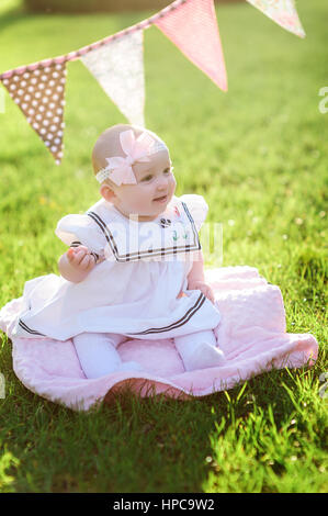 Petite fille en robe blanche assise sur l'herbe dans le parc Banque D'Images