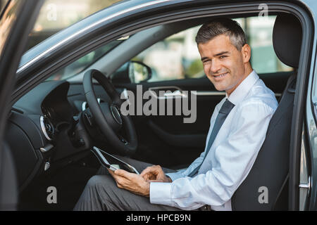 Homme d'affaires voyageant en voiture et naviguer avec son écran tactile, il est smiling at camera Banque D'Images