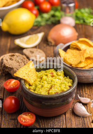 Guacamole au bol brun avec des croustilles sur le bureau en bois. Banque D'Images