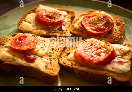 Fromage fondu sur du pain grillé avec des tranches de tomate et fines herbes Banque D'Images