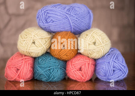 Eight skeins of lavender, gold, turquoise, cream and pink yarn stacked in a pyramid on a wood table. A stone wall is in background. Banque D'Images