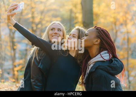 Trois jolies femmes qui en selfies autumn park. Jolies filles avec différentes couleurs de peau. Femme making funny faces and smiling at camera Banque D'Images