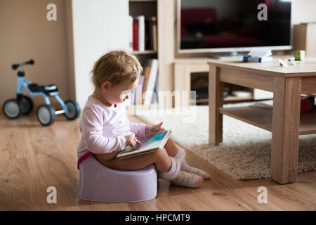 Cute little baby girl à la maison assis sur le pot à jouer avec tablet Banque D'Images