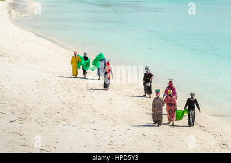 Zanzibar, Tanzanie - 4 novembre 2016 : Les femmes avec des vêtements colorés à marcher le long de la plage de Nungwi transportant leurs pots et net avec de petits poissons sur la th Banque D'Images