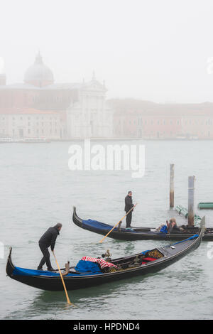 Deux gondoliers sont vu près de l'entrée de l'amarre à la place St Marc sur un jour brumeux à Venise. Cimitero di San Michele peut être vu dans t Banque D'Images