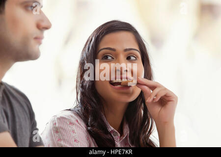 Woman biting un biscuit sourire à moitié à son mari Banque D'Images