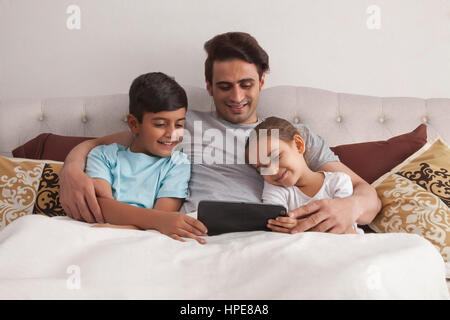 Le père et les enfants using digital tablet in bed