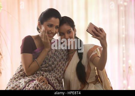 Smiling teenage daughter en sari et sa mère prenant selfies Banque D'Images