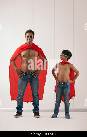 Jeune homme et garçon en costume de superman se dressant face Banque D'Images