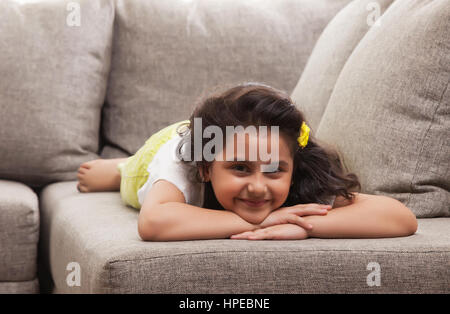 Smiling little girl est relaxant sur le canapé Banque D'Images