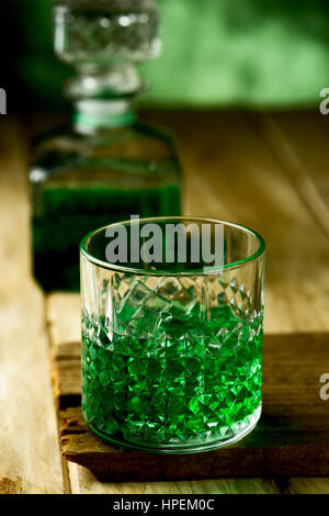 Libre d'un verre à whisky teint en vert sur une surface rustique en bois et une bouteille d'alcool avec teint en vert dans l'arrière-plan Banque D'Images