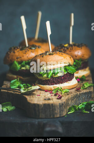 Burger végétalien sain de betterave et le quinoa patty, roquette, sauce à l'avocat et de farine de pain sur planche de bois rustique sur fond sombre, sélective Banque D'Images