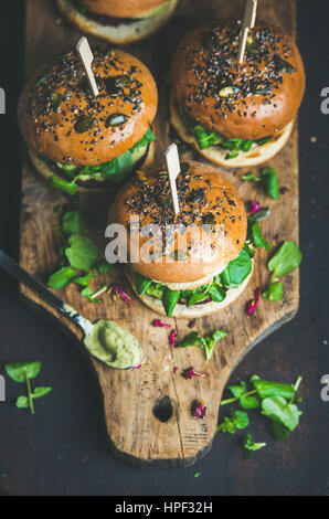 Burgers végétaliens sains de betterave et le quinoa patty, roquette, sauce à l'avocat, les bun sur planche de bois rustique sur fond sombre, les fo Banque D'Images