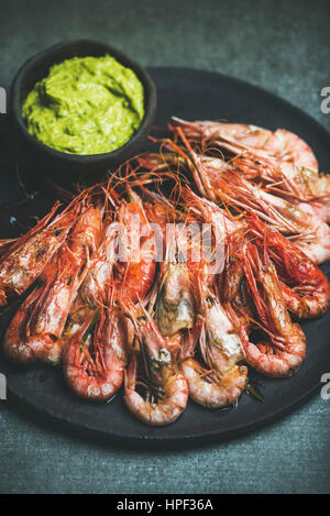 Crevettes rouges grillés avec sauce guacamole avocat en ardoise plaque noire sur fond de béton gris, selective focus Banque D'Images