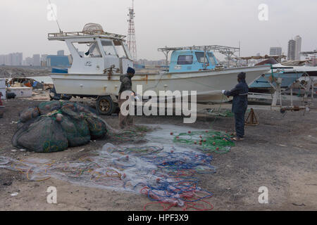 Les pêcheurs migrants travaillant sur des moustiquaires dans un port au Koweït. Banque D'Images