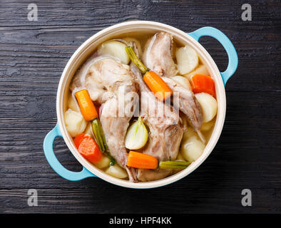 Compotée de Lapin aux pommes de terre et de carottes à poêle en fonte noire sur fond de bois brûlé Banque D'Images