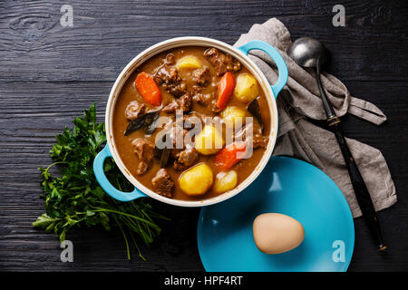 La viande de boeuf en ragoût avec des pommes de terre, les carottes et les épices dans poêle en fonte sur fond de bois noir brûlé Banque D'Images