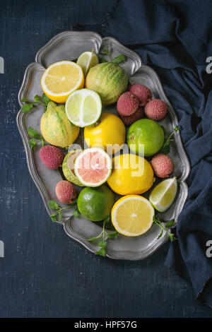 Variété d'agrumes entières et tranchées tigre rose citron, citron, citron vert, menthe et de litchi exotiques sur plaque de métal avec du vintage sur bleu foncé peut Banque D'Images