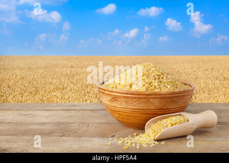 Le bulgur ou couscous dans un bol. grains de blé en sac. Bol en céramique dans bulgur sur table avec champ de blé sur l'arrière-plan. L'agriculture et de la récolte d'hiver Banque D'Images