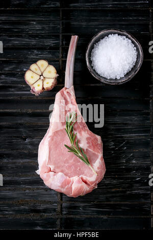 Veau crus Raw steak tomahawk avec de l'ail, le sel et l'assaisonnement sur la vieille grille de calandre noire sur fond de texture. Vue de dessus avec l'espace. Banque D'Images