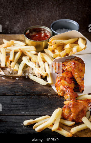 La restauration rapide de poulet frit les jambes, les ailes et les frites de pommes de terre dans des boîtes à lunch avec du sel et sauce ketchup servi sur du papier sulfurisé plus vieux ne sombre Banque D'Images