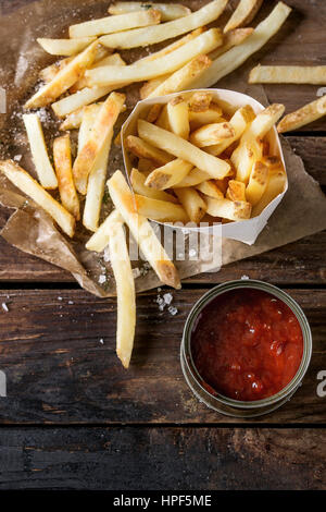 Restauration rapide avec la peau des pommes de terre frites servi avec du sel et du ketchup sauce en boîte à lunch sur du papier sulfurisé sur vieux fond en bois sombre. Vue de dessus, s Banque D'Images