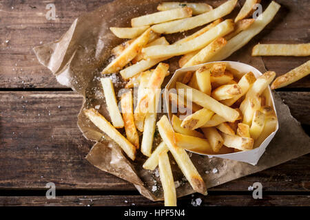 Restauration rapide avec la peau des pommes de terre frites servi avec du sel et des herbes dans le déjeuner fort sur du papier sulfurisé sur vieux fond en bois sombre. Vue de dessus, de l'espace pour Banque D'Images