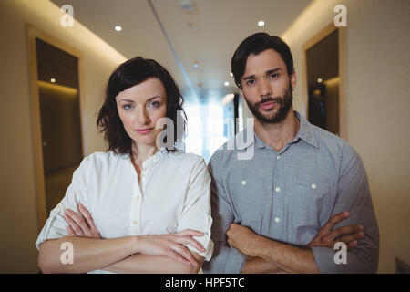 Portrait d'hommes et de femmes cadres d'standing with arms crossed in office corridor Banque D'Images