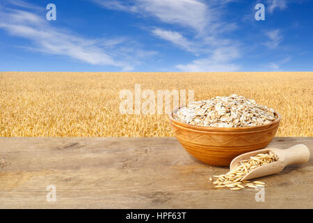 Flocons d'avoine dans un bol. Les grains d'avoine et avoine en écope dans un bol sur table en bois avec terrain sur l'arrière-plan. Champ d'or et bleu ciel. L'OGA non cuites Banque D'Images