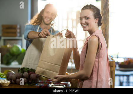 Portrait d'un vendeur de remettre un sac de légumes pour femme at grocery store Banque D'Images