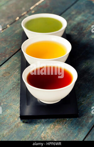 Concept de thé. Différents types de thé (noir, vert et thé matcha) dans des bols en céramique sur fond de bois