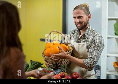 Smiling vendeur offrant des oranges à la femme au comptoir d'épicerie Banque D'Images