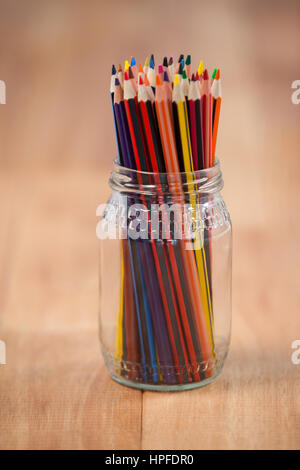 Crayons de couleur conservé dans un bocal de verre sur fond de bois Banque D'Images