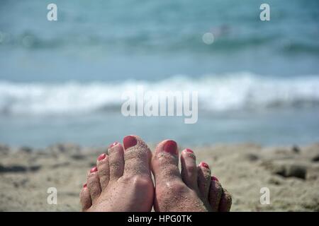 Pieds de sable avec des ongles rouges sur la plage avec la mer en arrière-plan flou Banque D'Images