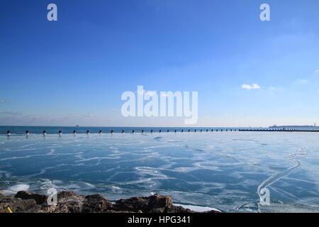 Vue sur poteaux de bois bordant l'horizon sur la glace d'un lac glacé et Chicago au bord du lac Michigan au cours d'un hiver glacial de janvier Banque D'Images