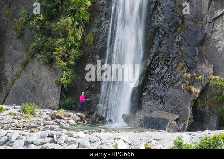 Franz Josef, Westland Tai Poutini National Park, côte ouest, Nouvelle-Zélande. Visiteur posant sous la cascade à Franz Josef Glacier Valley Track. Banque D'Images