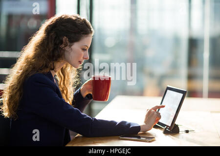 Businesswoman using digital table tout en ayant tasse de café in office Banque D'Images