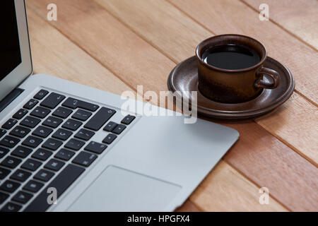 Tasse de café noir et de l'ordinateur portable sur fond de bois Banque D'Images