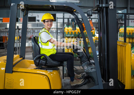 Portrait of smiling female factory worker driving forklift in factory Banque D'Images
