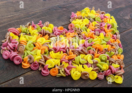 Pâtes colorées par les légumes colorés (Verts, betteraves, épinards, carottes, tomates, poivrons) sur une table en bois foncé en forme de coeur . Banque D'Images