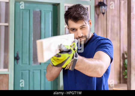 Carpenter concentré holding planche en bois dans les mains on porch Banque D'Images