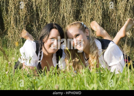 Parution du modèle , Zwei junge, attraktive Frauen im Dirndl liegen nebeneinander dans der Wiese - deux femmes se trouvant dans le pré Banque D'Images