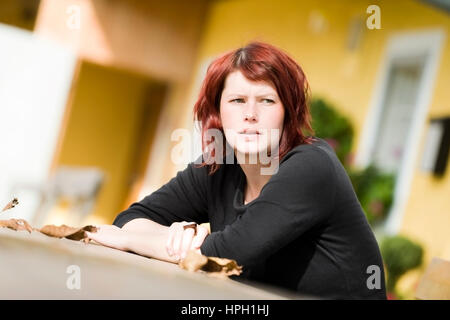 Parution du modèle , Junge, rothaarige Frau sitzt une einem Tisch - jeune femme aux cheveux rouges, Banque D'Images
