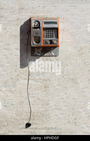 Vue de face vertical orange endommagés téléphone public avec de la casse combiné contre un mur blanc rayé Banque D'Images